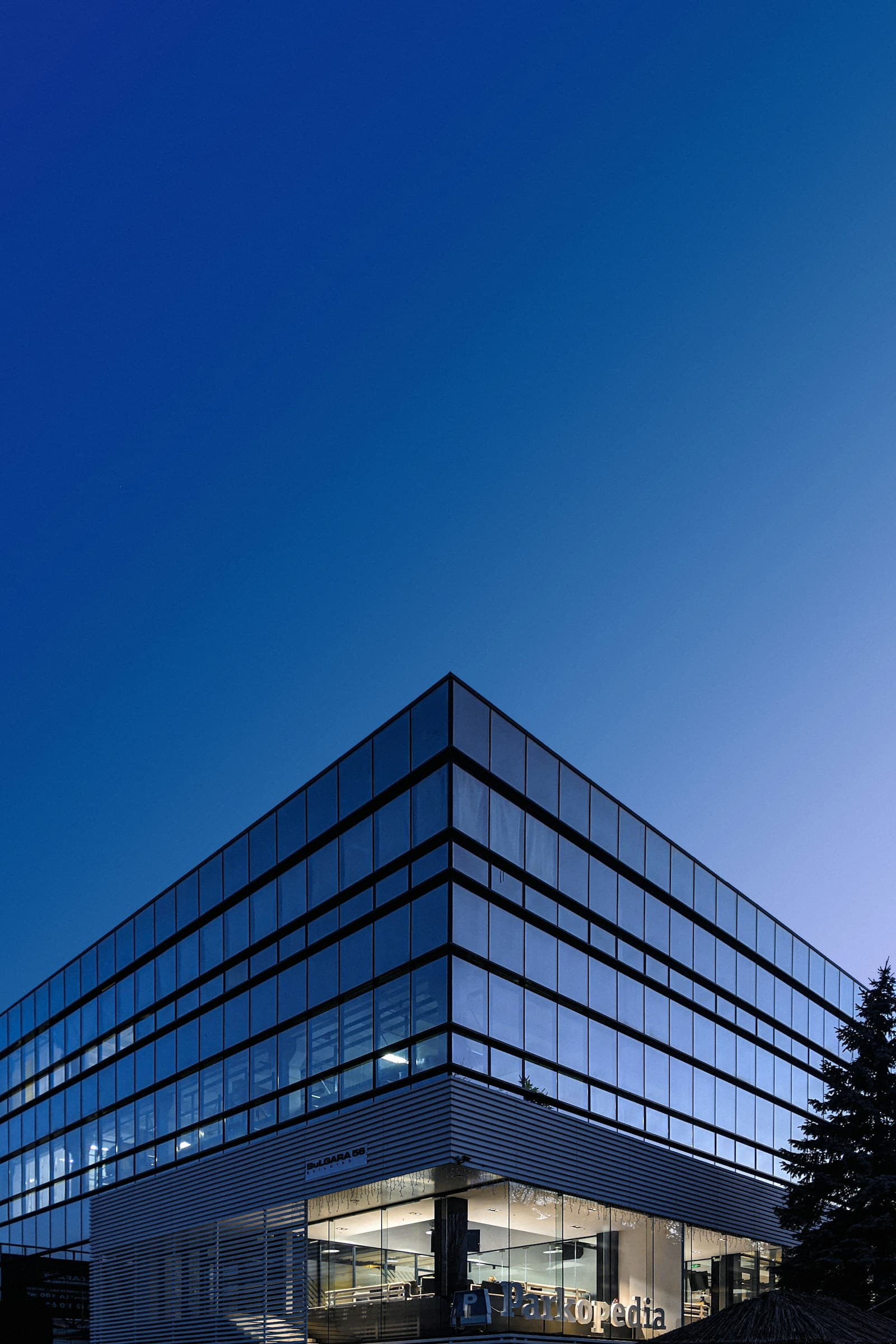 The corner of a glass office building against a deep blue sky